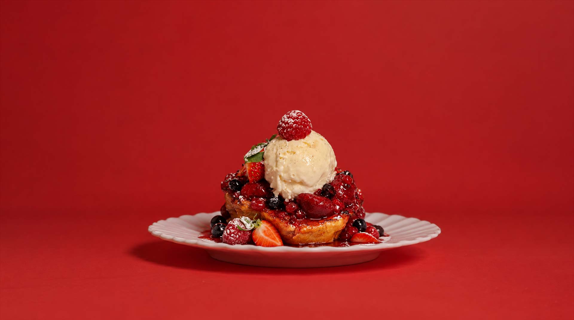 French toast med vaniljglass och färska bär på röd bakgrund
